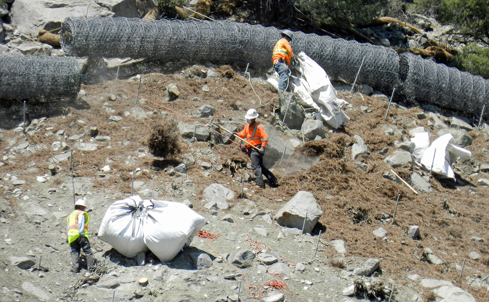 Erosion control/revegetation mixture is applied high on the roadcut slopes by hand. Photo by Sandra Noll.