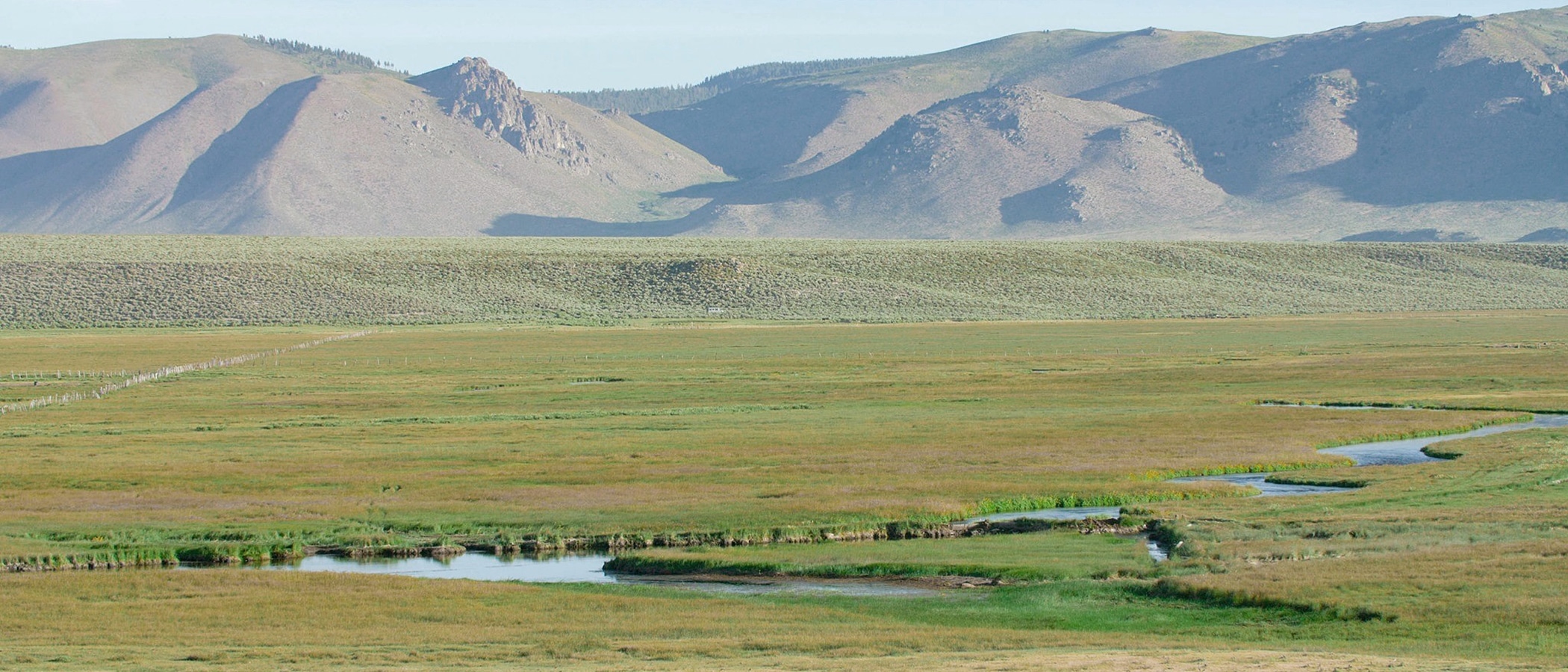 Bright green fields stretch into lighter hilly mountains. A winding river runs through the valley.