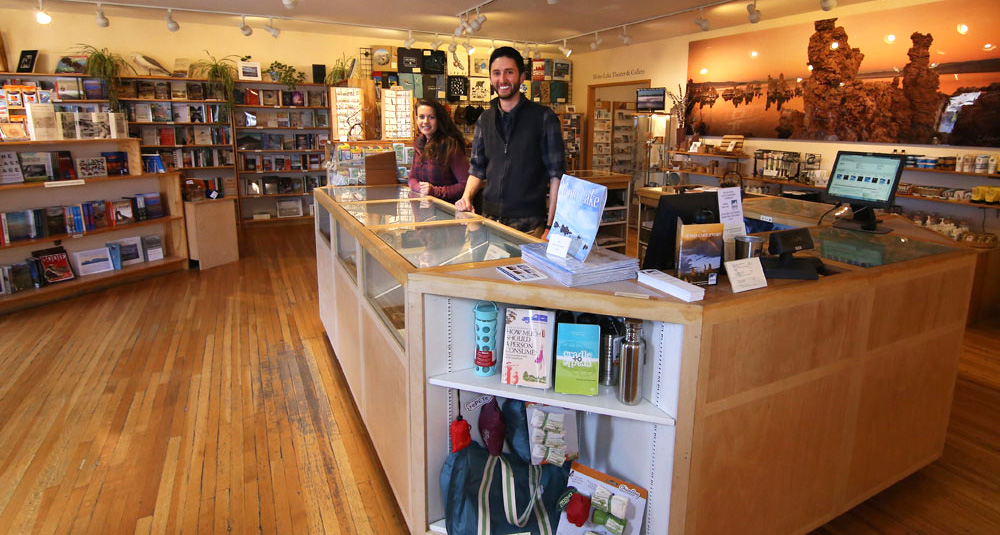 Two smiling people stand at the front counter inside the warm and welcoming Mono Lake Committe Information Center & Bookstore.