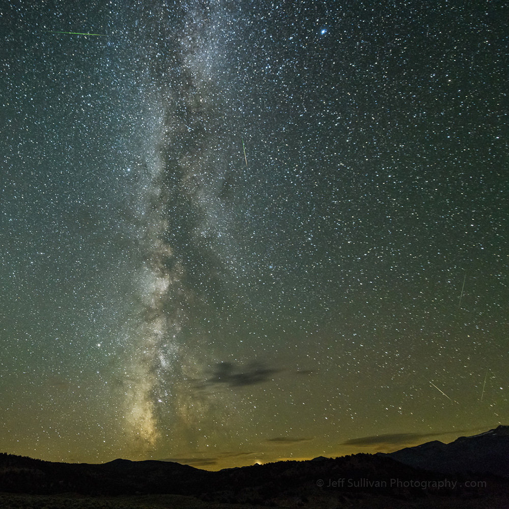 The milky way extends vertically in above the silhouettes of mountains with the last orange glow of light above them.