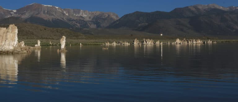 Glassy lake in front of Sierra Nevada with tufa towers reflecting in the morning light with one point of reflection in the lake from a mirror on a hill above.