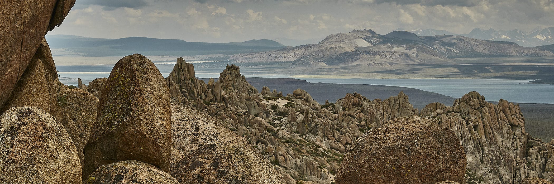 Unusually rounded granite rock piles and outcroppings in the foreground of a view out to Mono Lake with the Mono Crater plug domes in the distance.