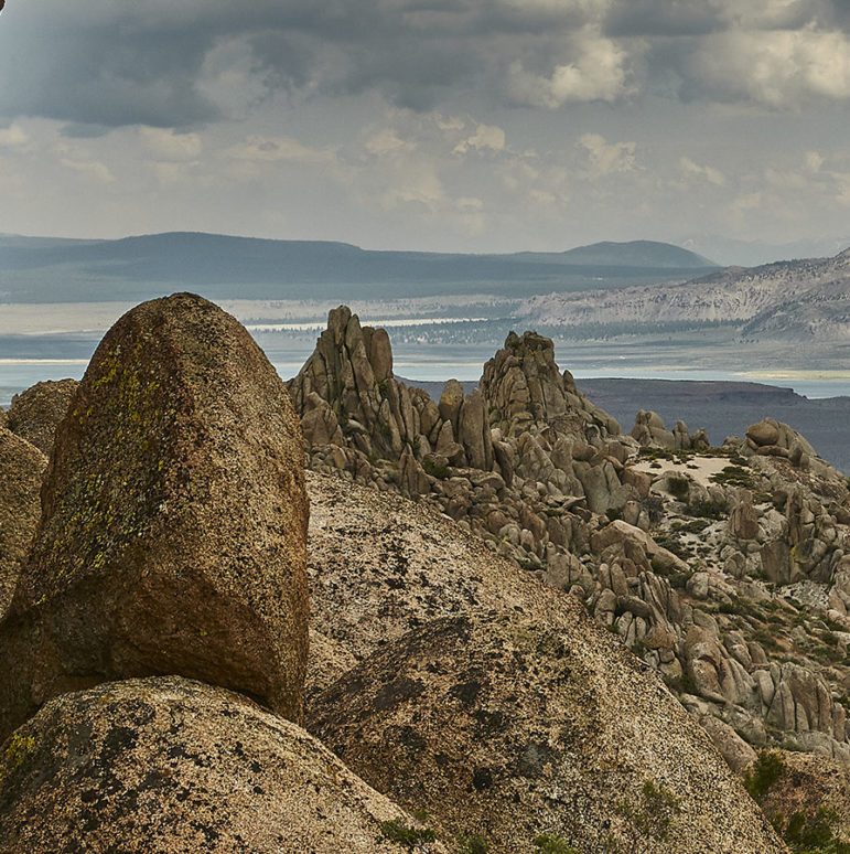 Unusually rounded granite rock piles and outcroppings in the foreground of a view out to Mono Lake with the Mono Crater plug domes in the distance.