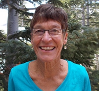 Woman smiling straight into the camera while standing in front of a fir tree.