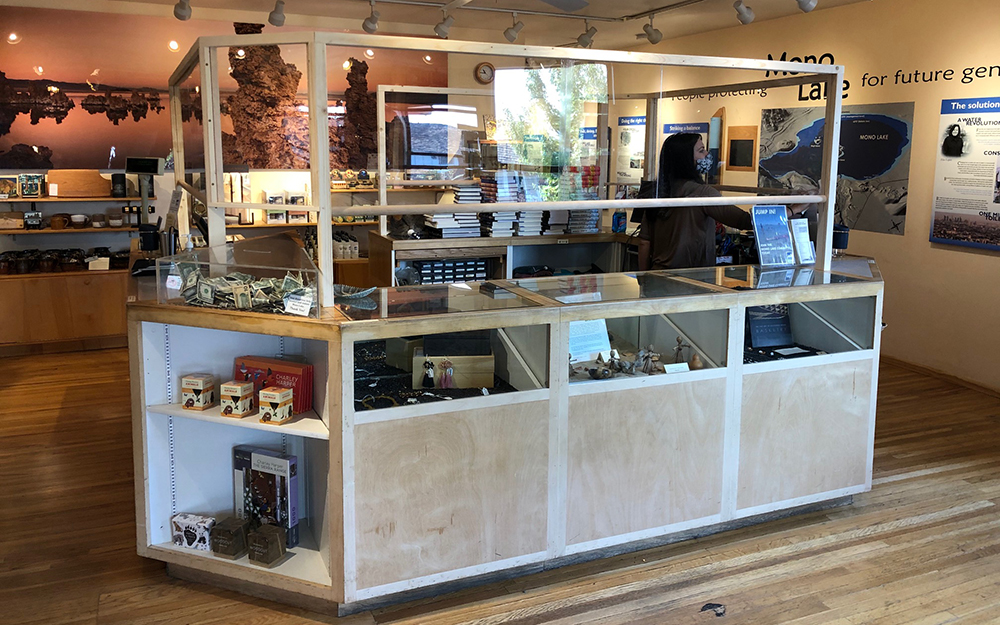 A booth in the Mono Lake Committee store is protected with see through plastic shields to promote Covid-19 safety. A worker inside wears a mask.