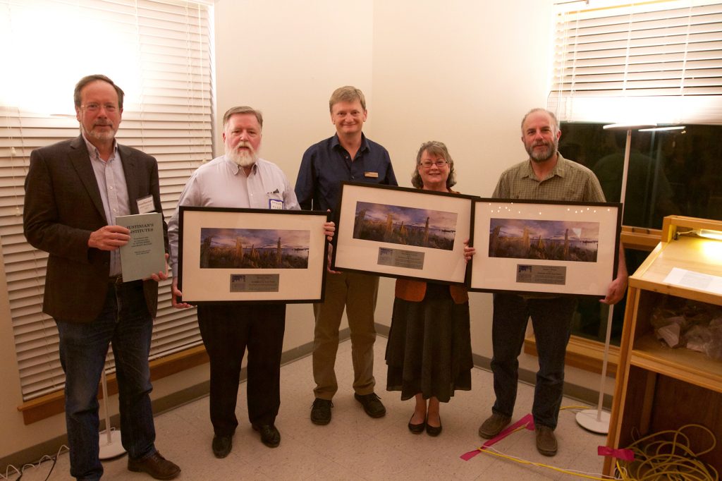 Four men and one woman stand smiling in a room, each holding framed pictures of the tufa at Mono Lake. The man to the left is holding a smaller book.