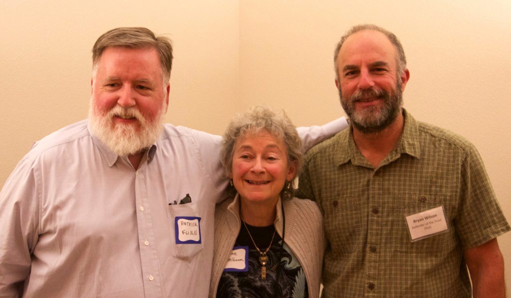 Two men put their arms around one woman and smile at the camera.