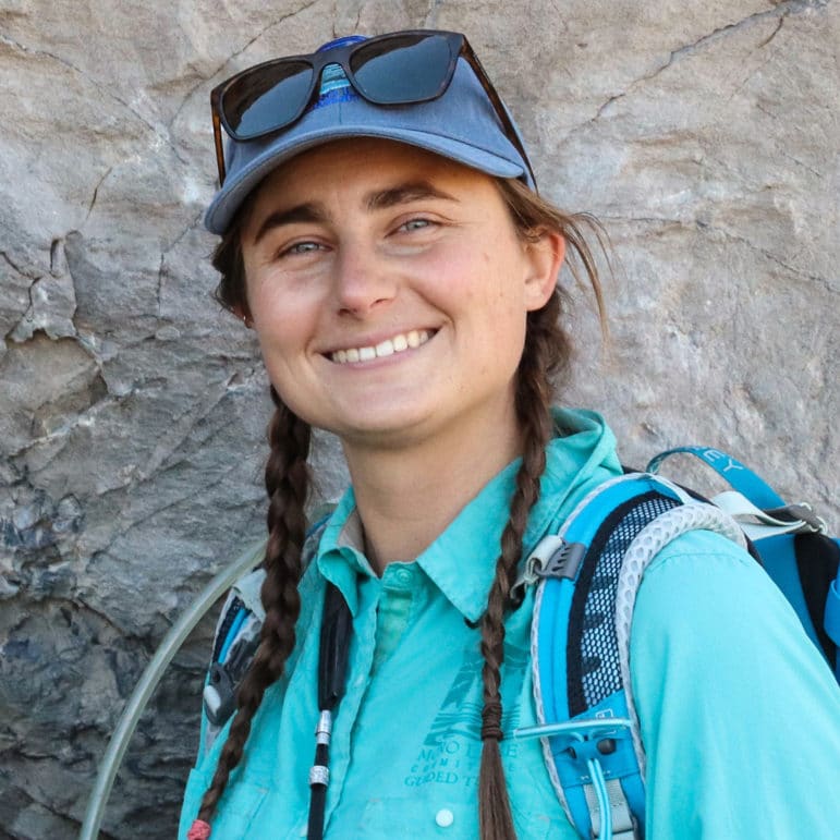 Nora Livingston in outdoor guiding gear pointing out a geologic feature on a rock.