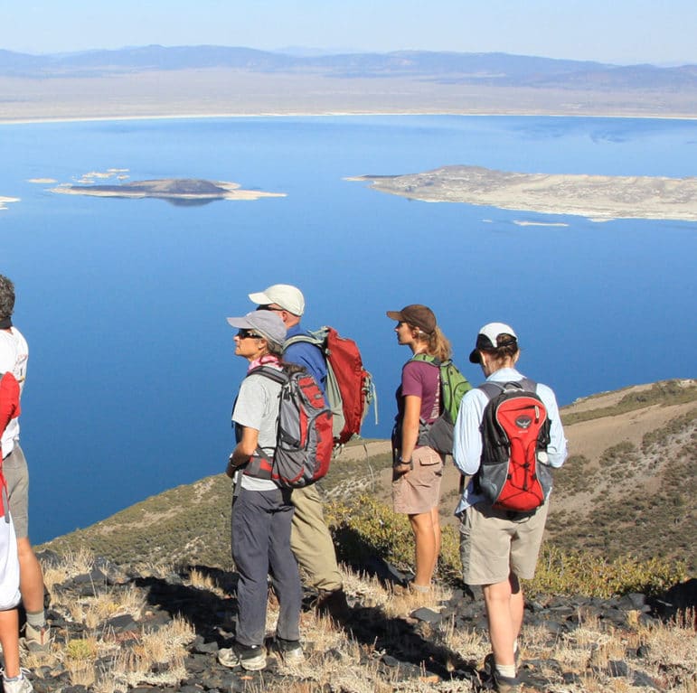 Nine people wearing backpacks and carrying binoculars on a promontory looking out over a dramatic overview of Mono Lake.