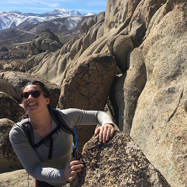 Lily Pastel smiling while hiking in a rocky desert landscape.