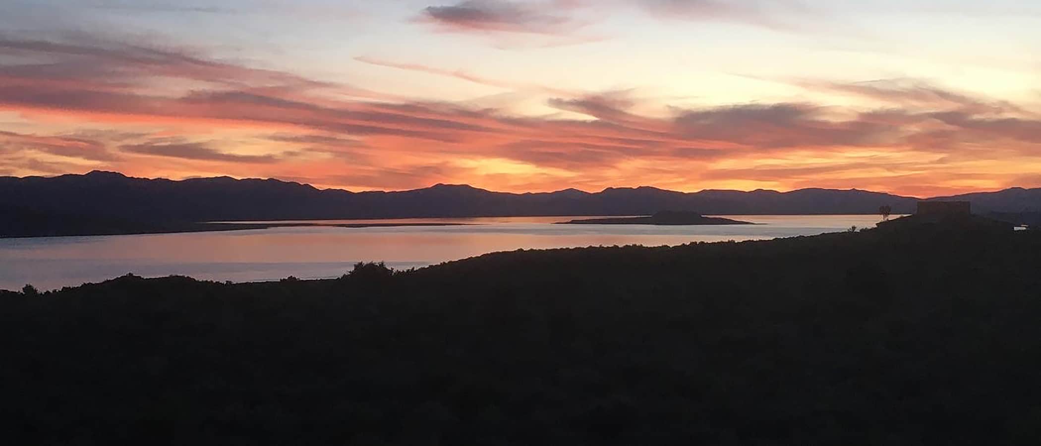 Coral pink and orange sunset stretches across the sky above silhouetted mountains and Mono Lake.