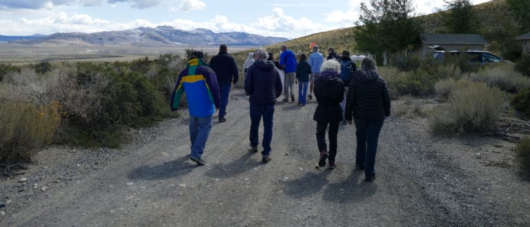 A group of about 12 people wearing cool-weather jackets walking on a dirt road near the site of the Tioga Inn development project.