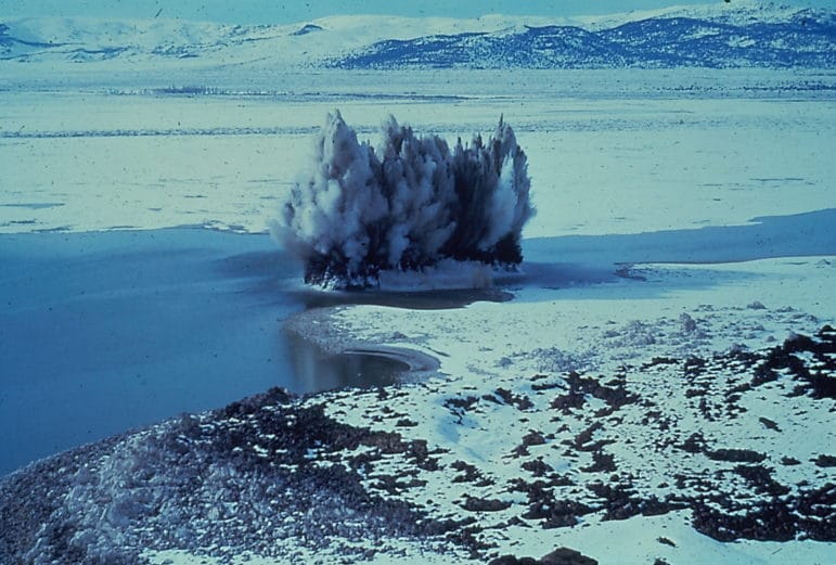 Aerial view of the landbridge to the nesting colony of California Gulls at Mono Lake being dynomited with mud and water flying high into the air.