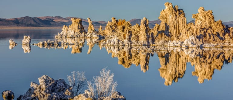 Brightly lit tufa towers reflecting in a perfectly glassy Mono Lake.