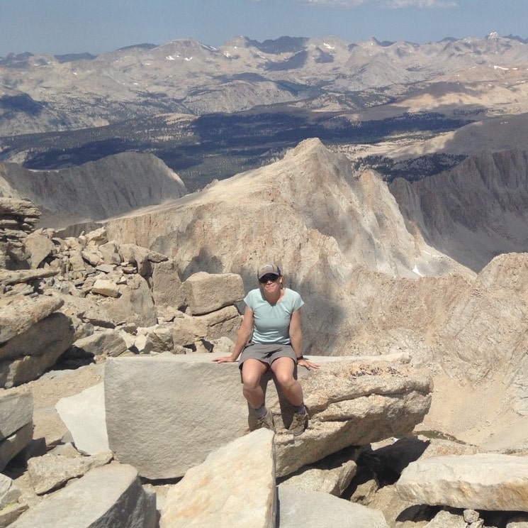 Maureen McGlinchy sitting on a large piece of granite surrounded by Sierra peaks in the background.