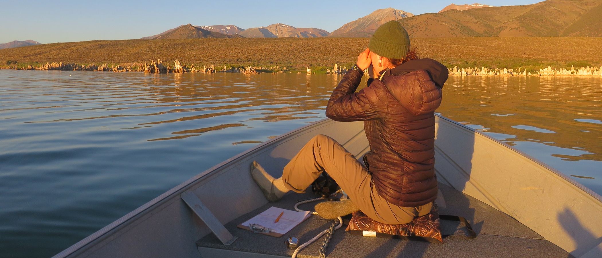 Person sitting on a boat looking out at Mono Lake in the early morning sun with the mountains in the background.