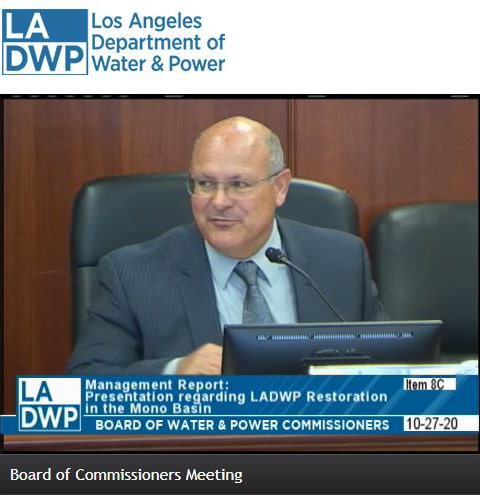 A screenshot from the Board of Commissioners Meeting shows a bald man in a suit speaking.