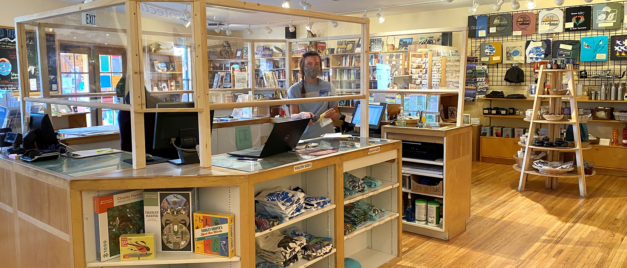 A cheerful employee wearing a mask stands in the store behind clear plastic for Covid-19 safety.