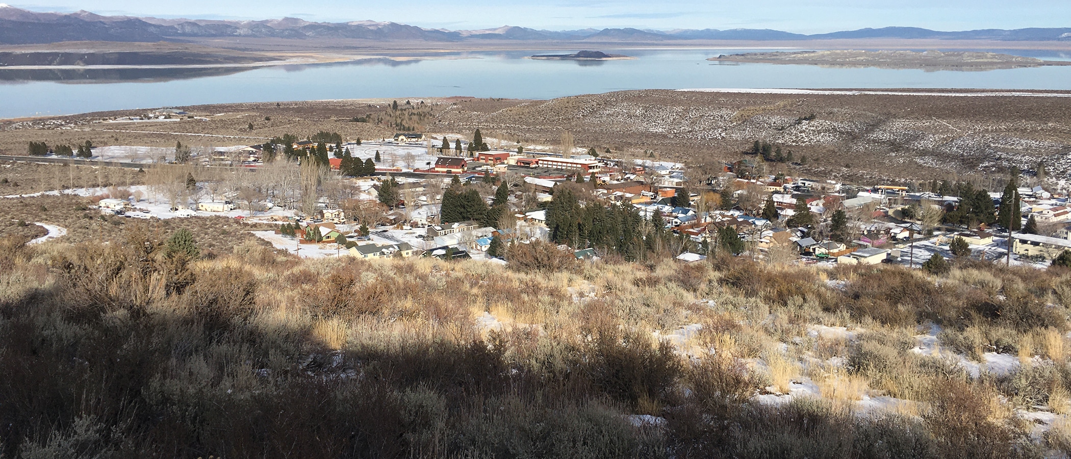 A birds eye view of Lee Vining buildings from a hill shows Mono Lake in the distance.