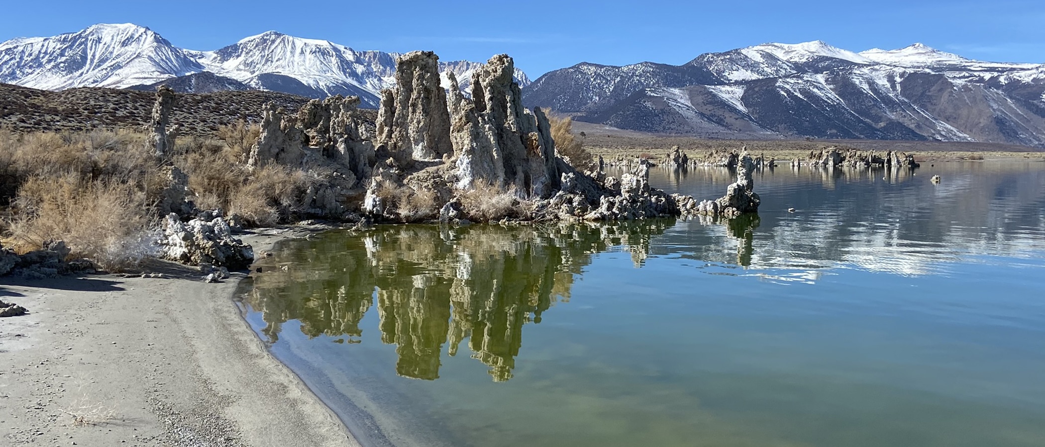 Tufa towers stand tall in turquoise Mono Lake water, with snowcapped Sierra Nevada mountains behind it.