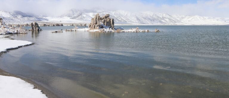 Snowy tufa towers and mountains loom in gray greed rippling lake water.