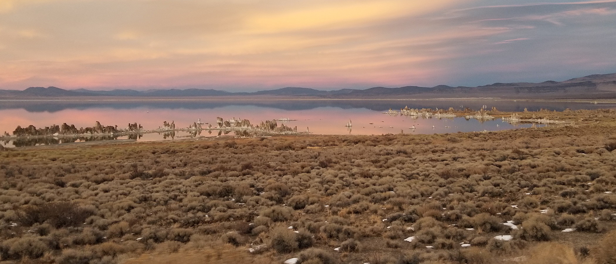 Sagebrush ringing a lake filled with tufa reflecting evening colors from clouds.