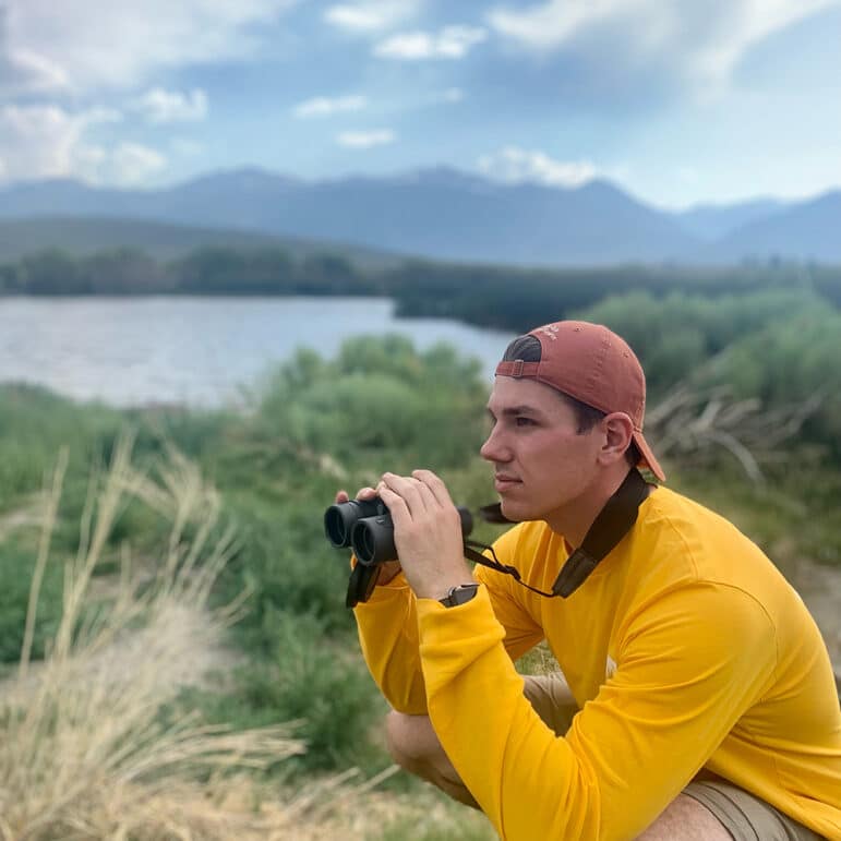 Person in a yellow shirt holding binoculars looking in the distance.