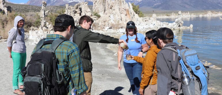 People on the shore of Mono Lake near tufa pouring water from one container into another.