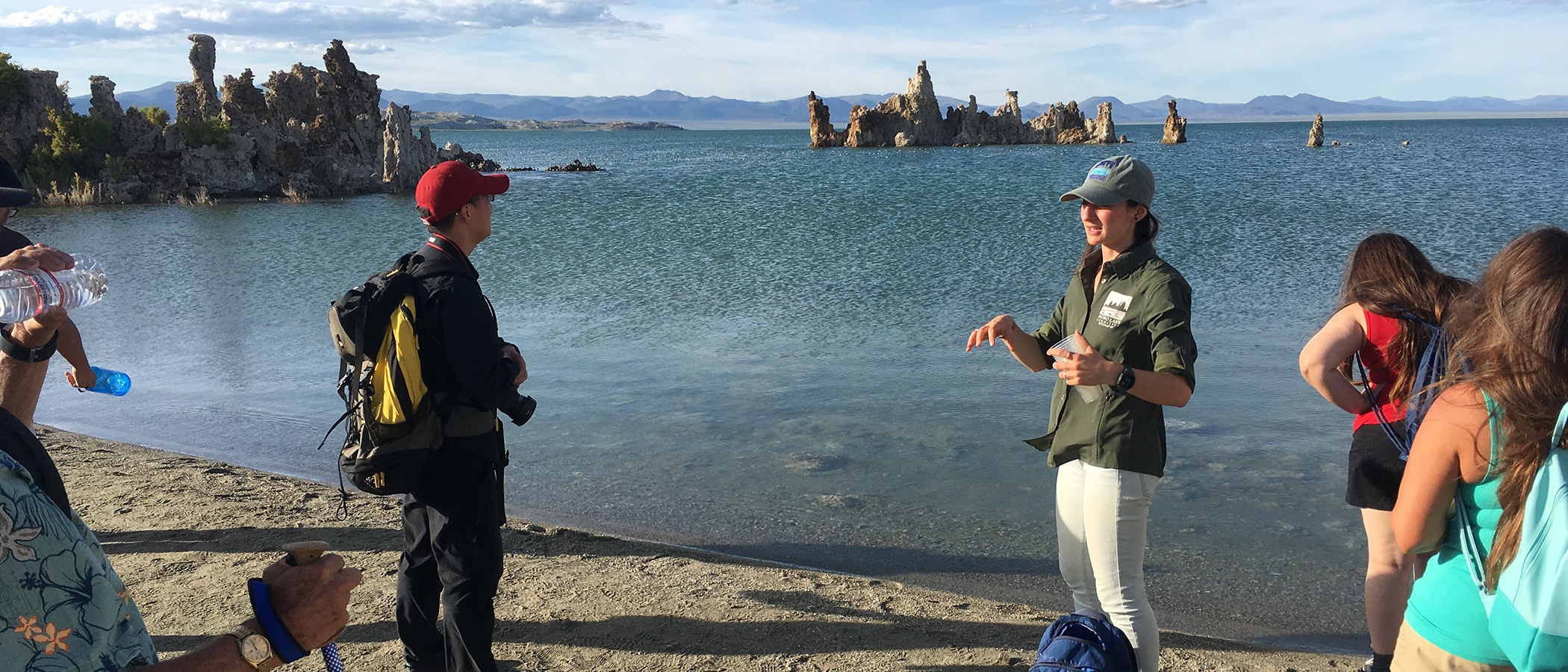 Mono Lake Committee staffer standing with their back to Mono Lake talking to a tour group, tufa and scattered clouds are in the background.