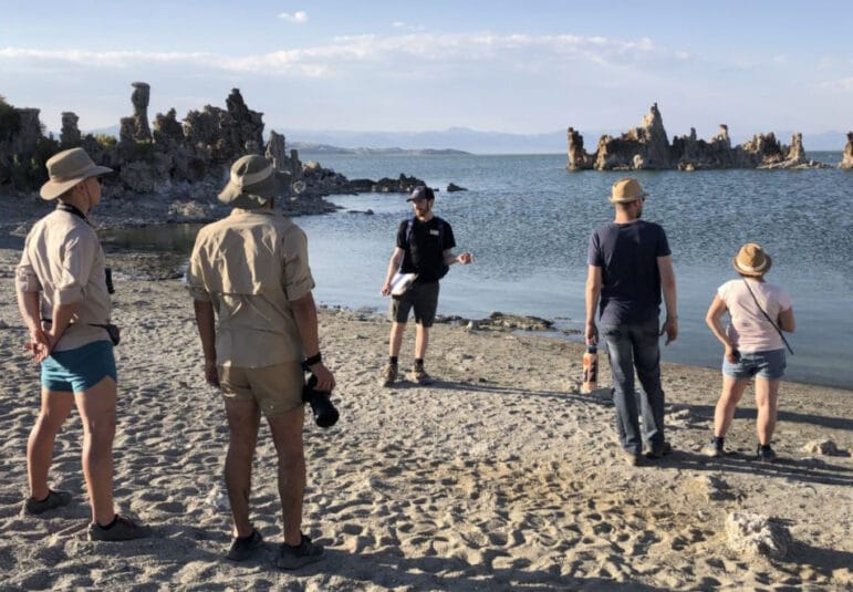 Mono Lake Committee staffer standing with their back to Mono Lake talking to a tour group, tufa and scattered clouds are in the background.