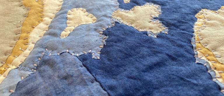 Patches of blue and tan fabric are stitched together in this closeup of a quilt.