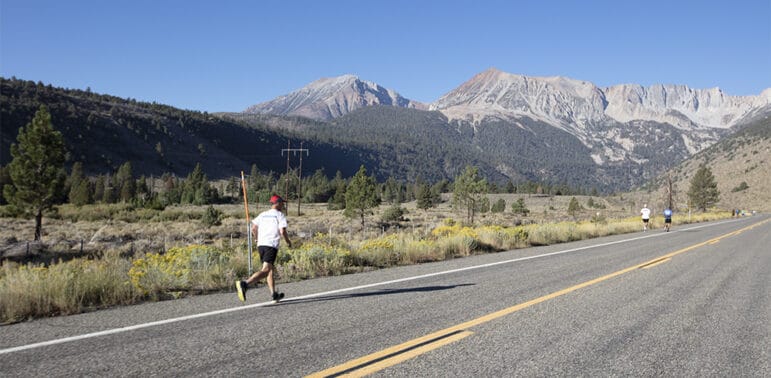 Several people running along the edge of a paved road with granite mountain peaks in the distance.