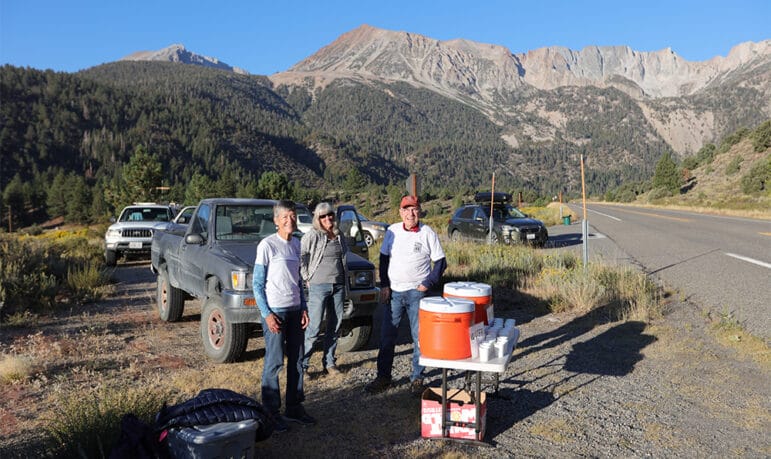 Volunteers staffing a race aid station along a paved road with mountains in the background.