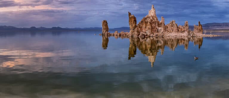 Glassy surface of Mono Lake with tufa reflecting and clouds in the sky.