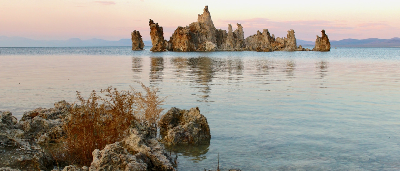 Tufa sits surrounded by lake against pink and purple skies.