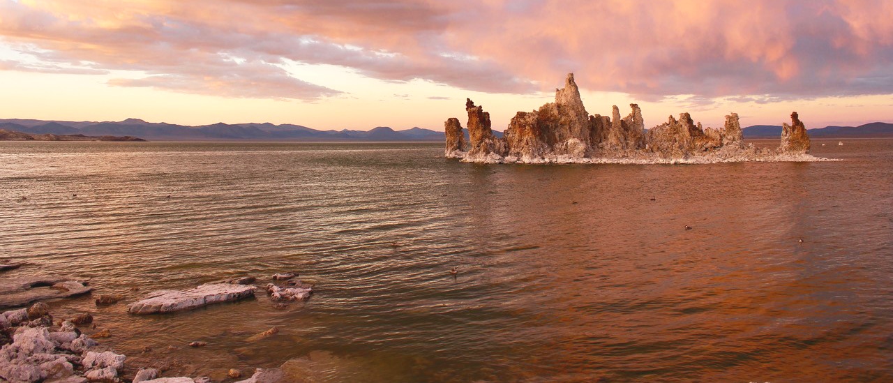 Tufa sits surrounded by lake against pink and purple skies.